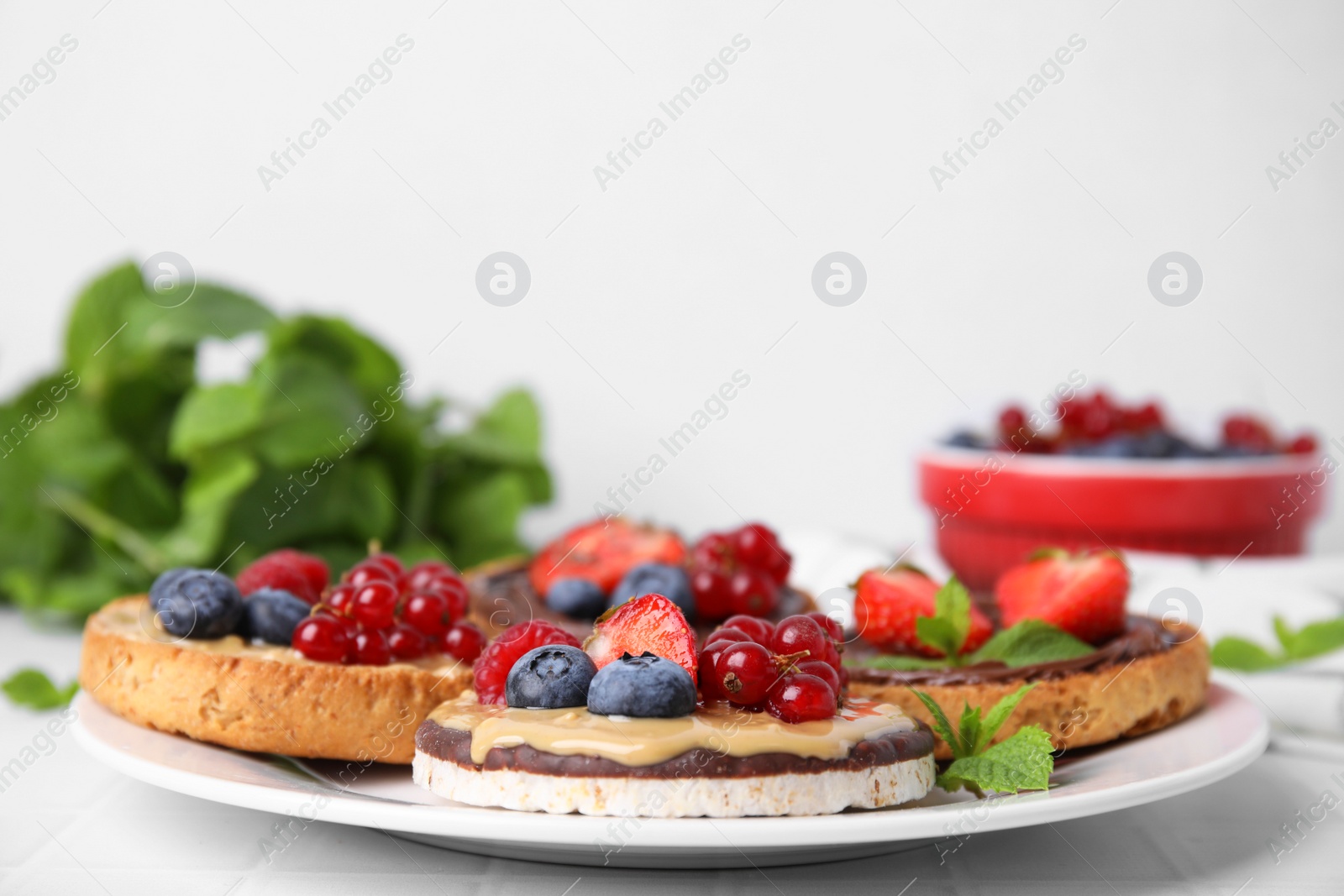 Photo of Fresh rice cake and rusks with different toppings served on white table, closeup