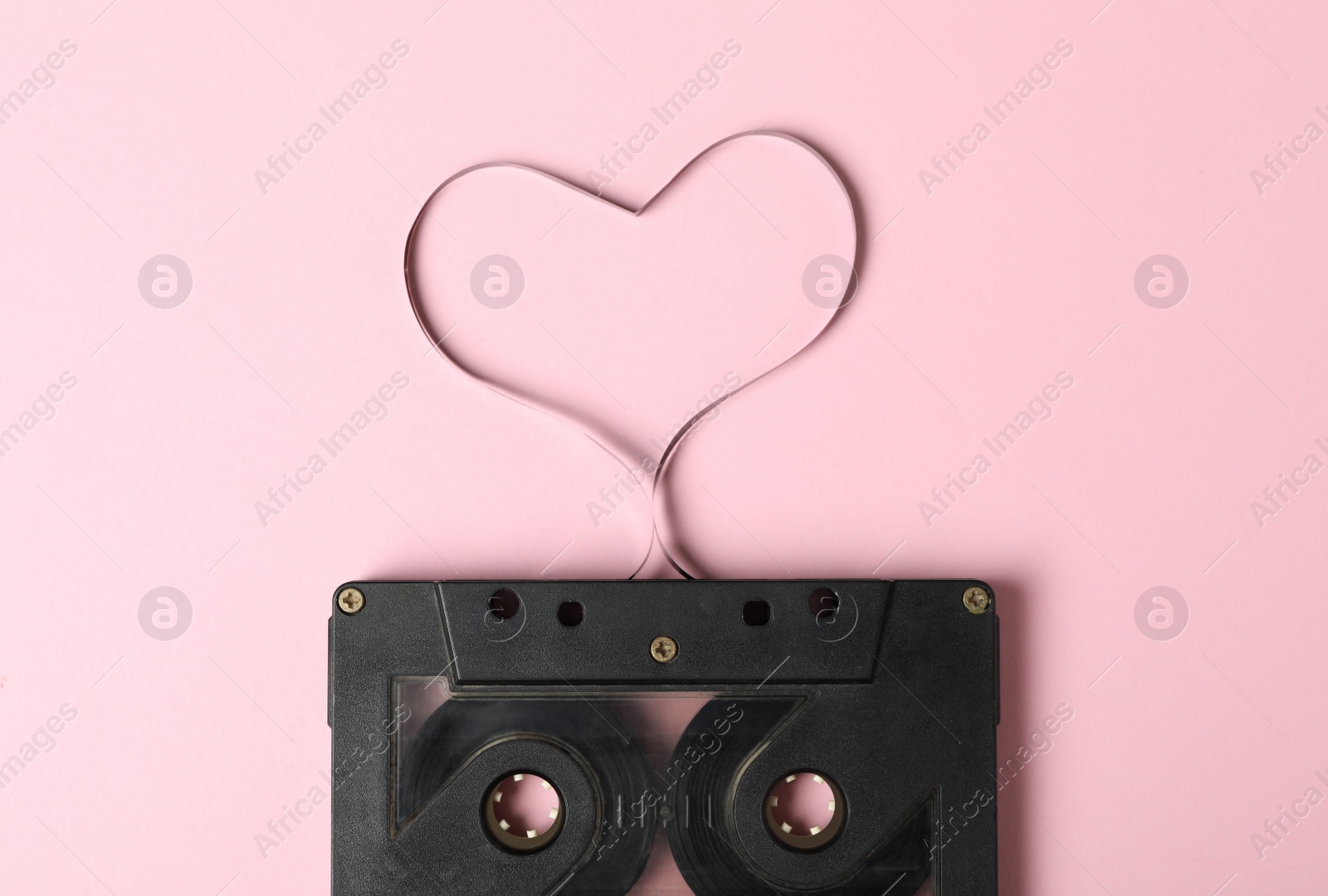 Photo of Music cassette and heart made with tape on pink background, top view. Listening love song