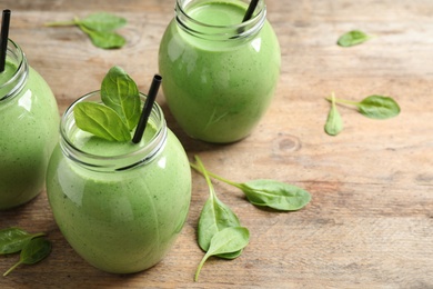 Jars of healthy green smoothie with fresh spinach on wooden table. Space for text