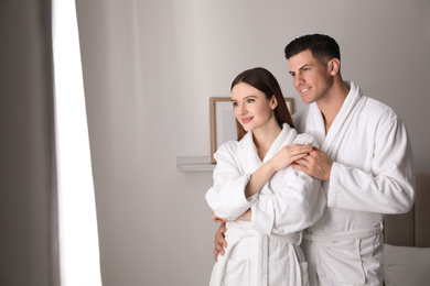 Happy couple wearing bathrobes near window in room