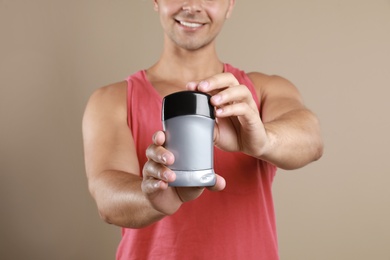 Young man holding deodorant on beige background, closeup. Mockup for design