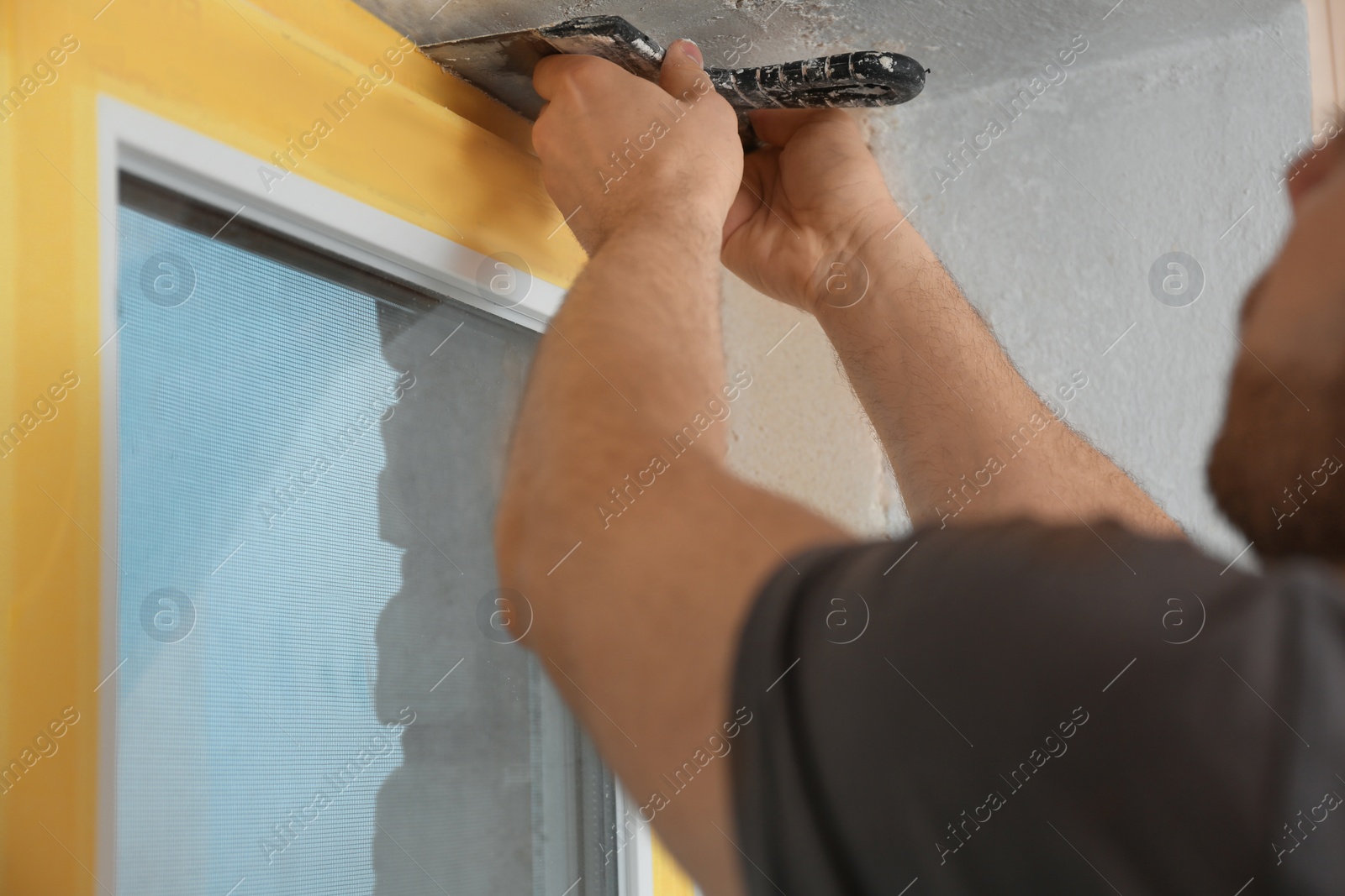 Photo of Man plastering window area with putty knife indoors, closeup. Interior repair