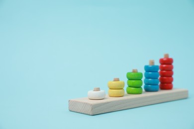 Photo of Stacking and counting game wooden pieces on light blue background, space for text. Educational toy for motor skills development