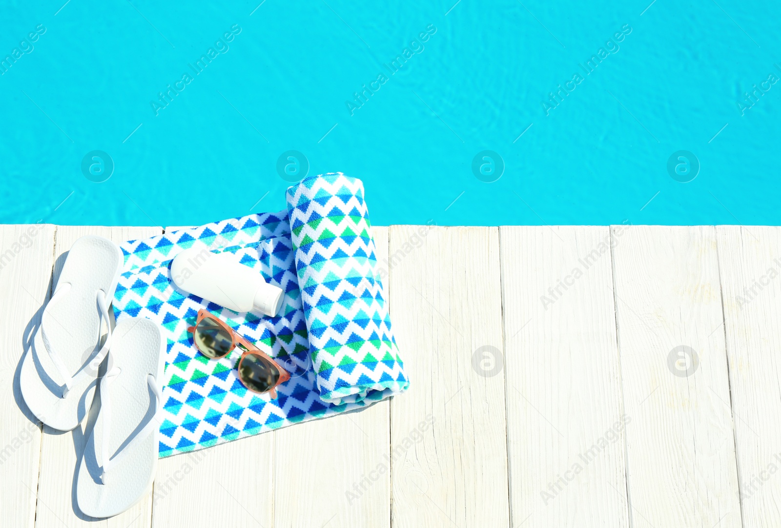Photo of Beach accessories on wooden deck near swimming pool, top view. Space for text