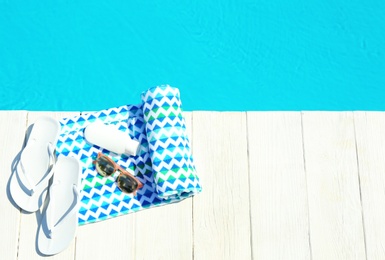 Beach accessories on wooden deck near swimming pool, top view. Space for text