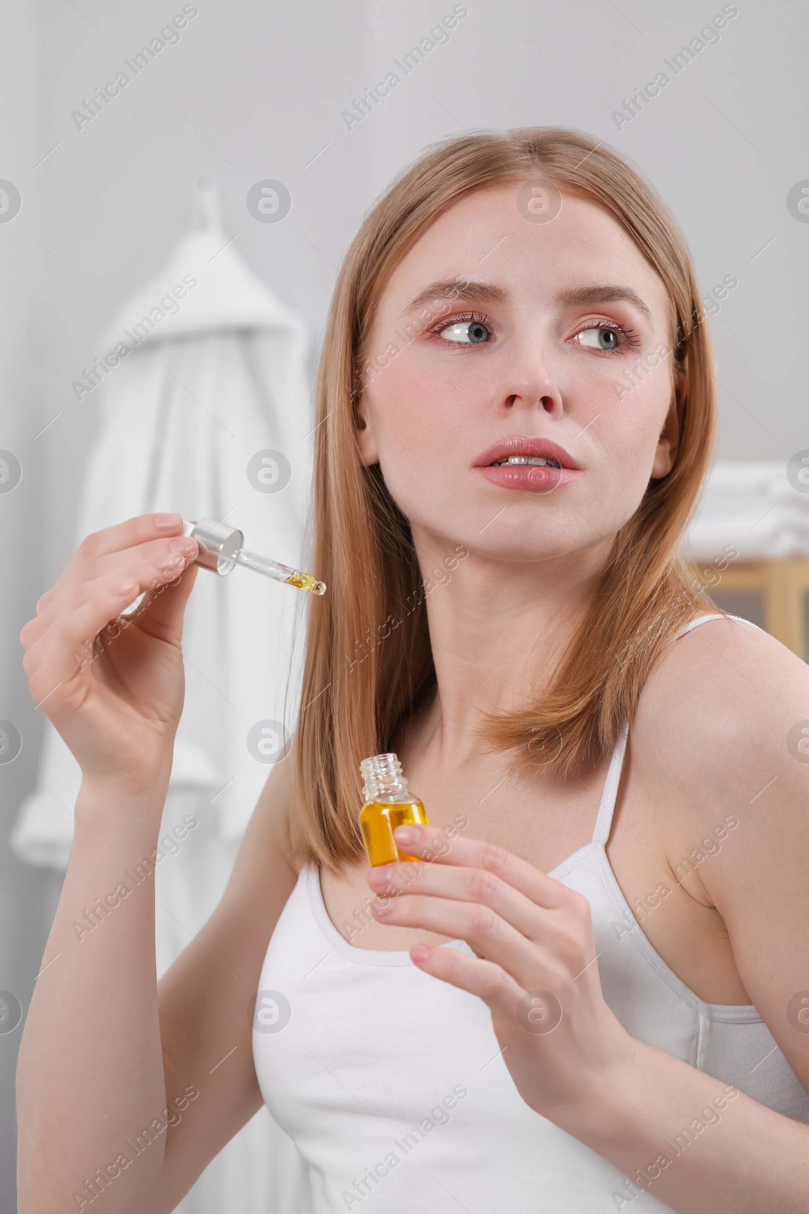 Photo of Young woman with bottle of essential oil in bathroom