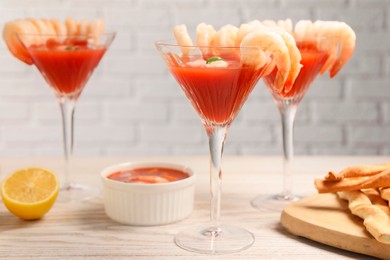 Photo of Tasty shrimp cocktail with sauce in glasses and lemon on light wooden table