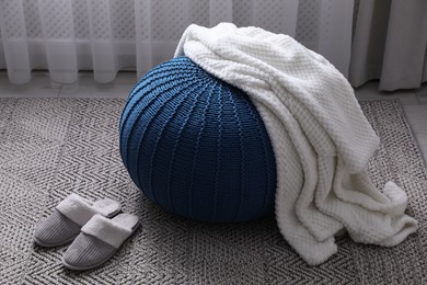 Soft blanket on stylish blue pouf and slippers in room