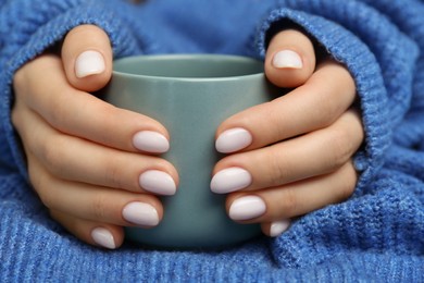 Woman with white nail polish holding cup, closeup
