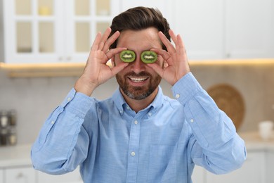 Photo of Smiling man holding halves of kiwi near his eyes indoors