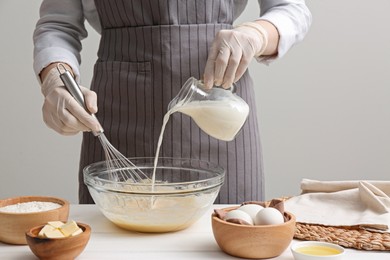 Photo of Woman whisking crepe batter in glass bowl at white wooden table, closeup