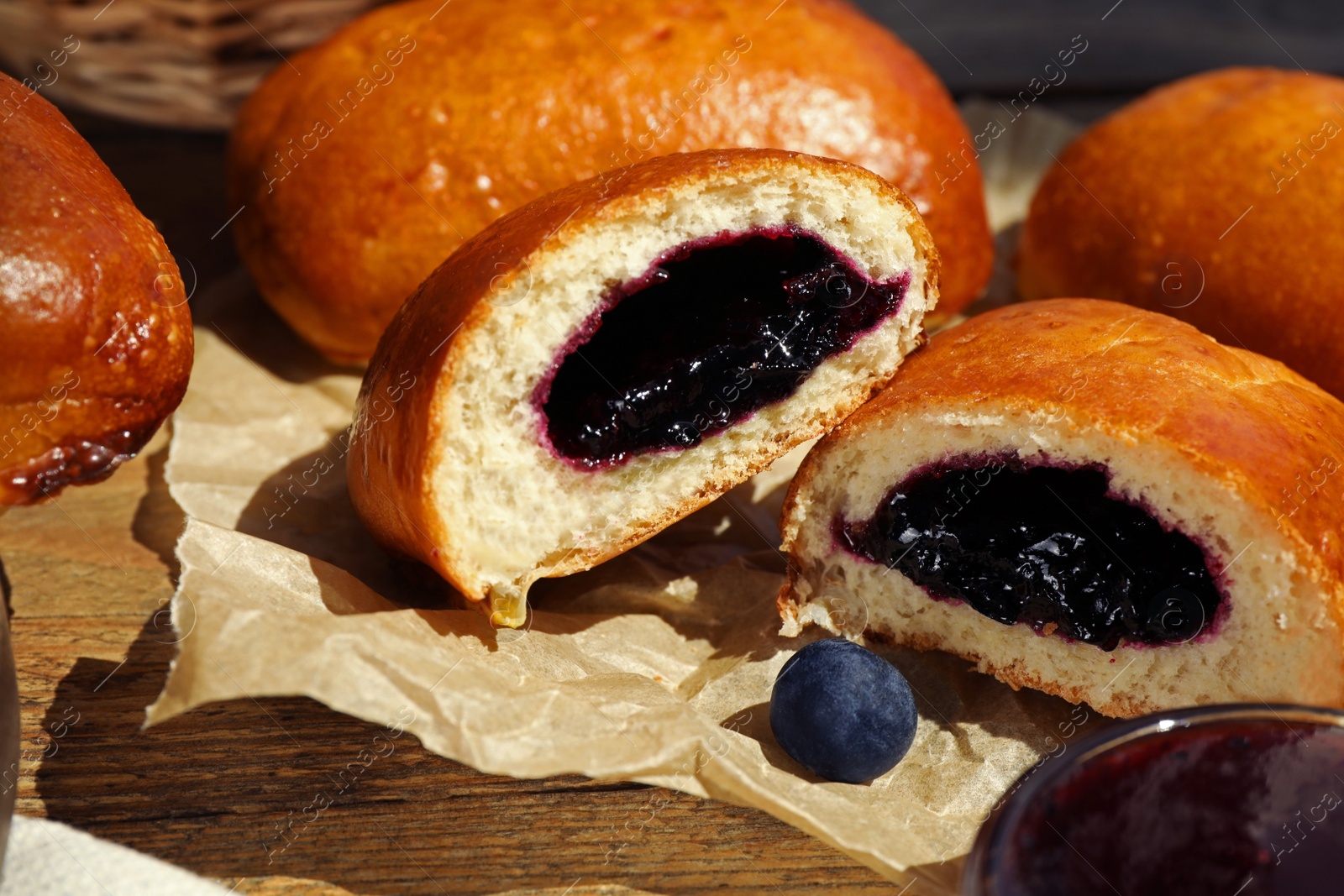 Photo of Delicious baked patties with jam and blueberries on wooden table, closeup