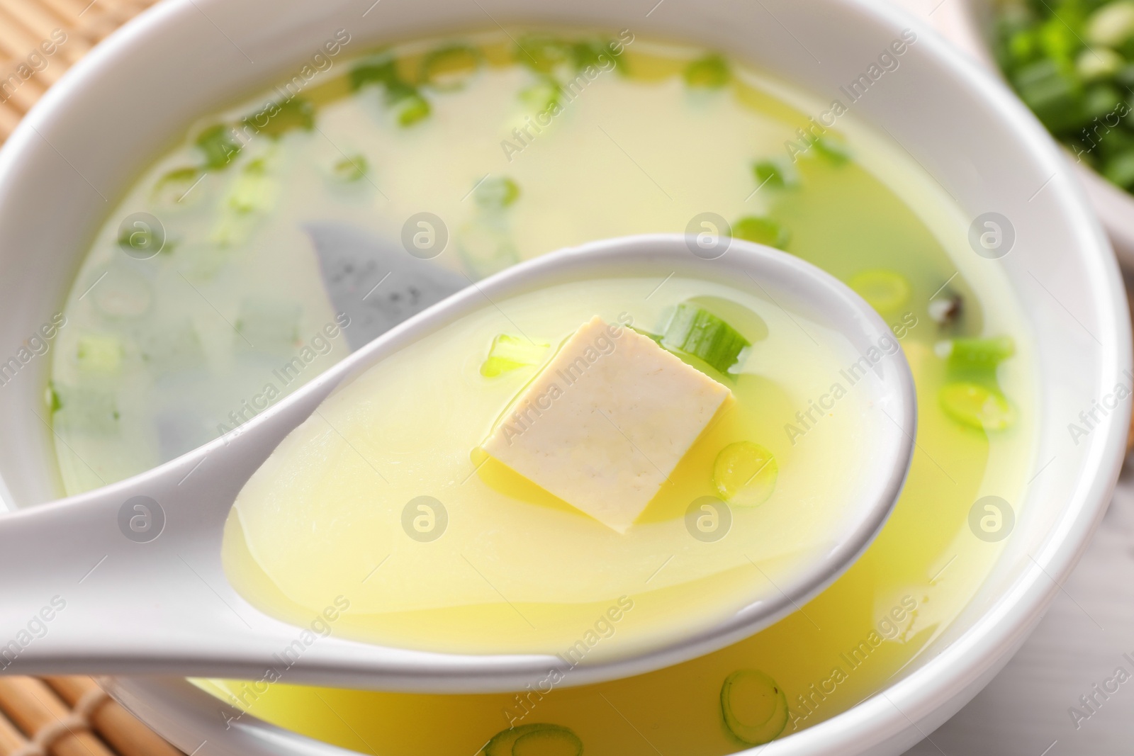 Photo of Eating delicious miso soup with tofu from bowl on table, closeup