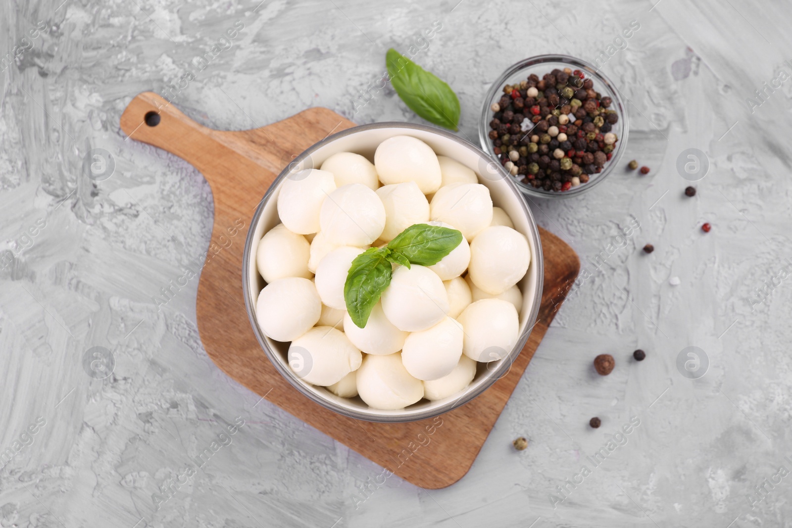 Photo of Tasty mozzarella balls and basil leaves in bowl on grey table, flat lay