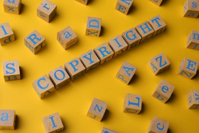 Photo of Plagiarism concept. Word Copyright made of wooden cubes with letters on yellow background