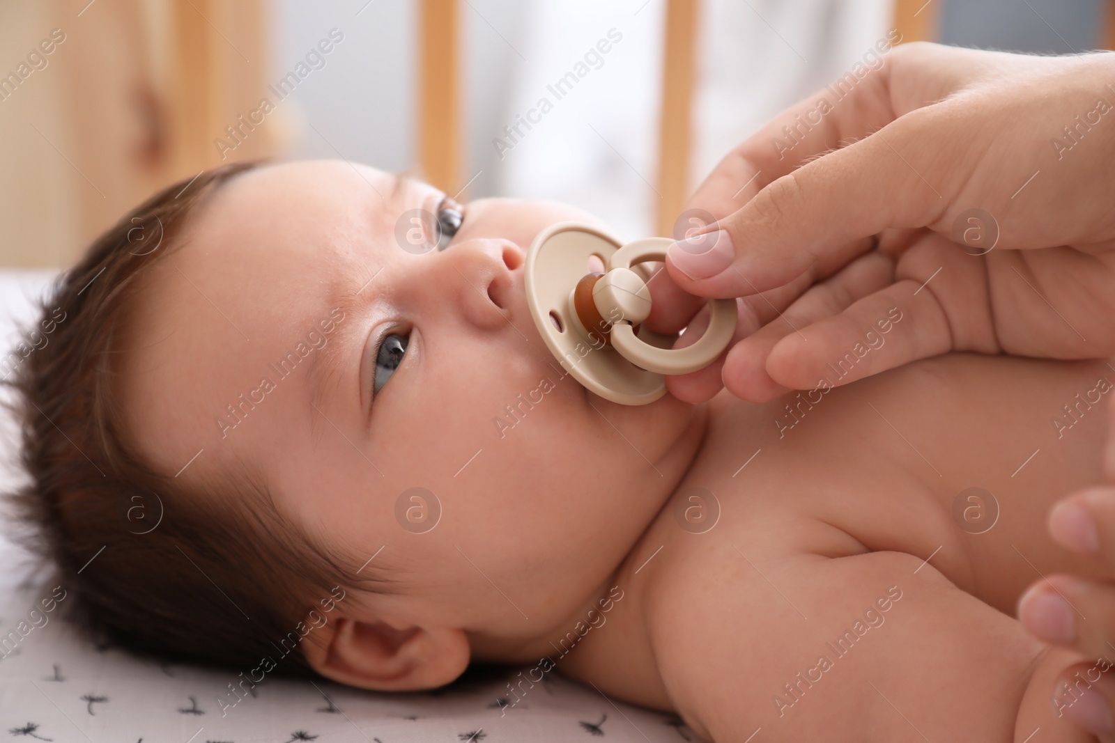 Photo of Mother giving pacifier to her cute little baby in crib at home, closeup