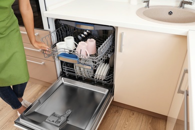 Young woman loading dishwasher in kitchen, closeup. Cleaning chores