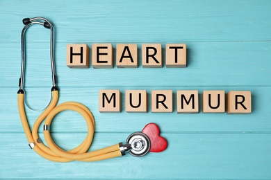 Photo of Wooden cubes with text Heart Murmur and stethoscope on blue wooden background, flat lay