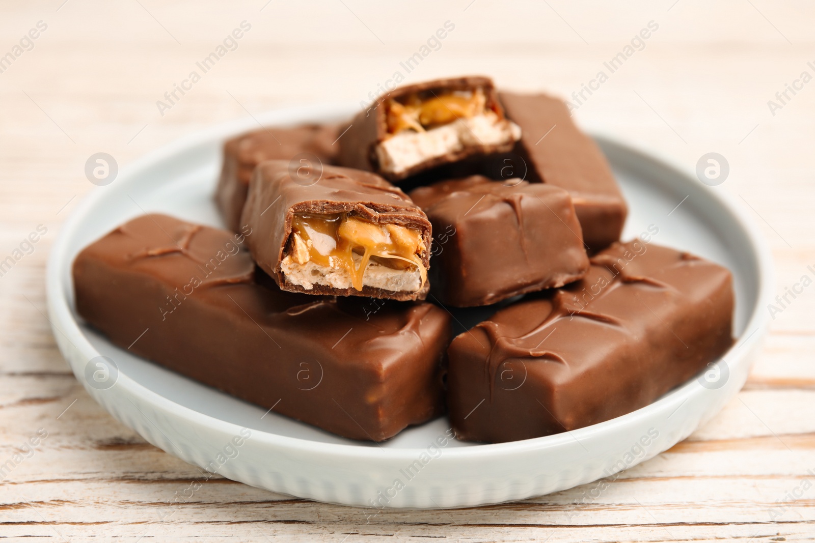 Photo of Plate of chocolate bars with caramel, nuts and nougat on white wooden table, closeup