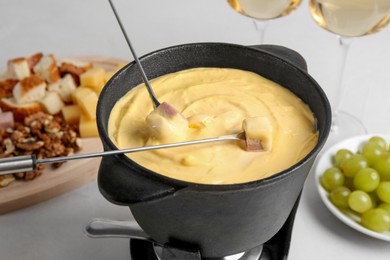 Dipping ham into fondue pot with tasty melted cheese at white table, closeup