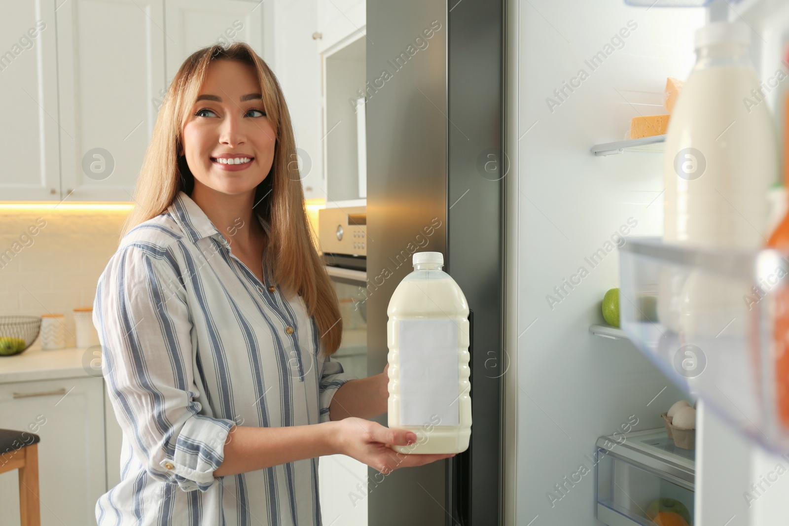 Photo of Young woman with gallon of milk near refrigerator in kitchen