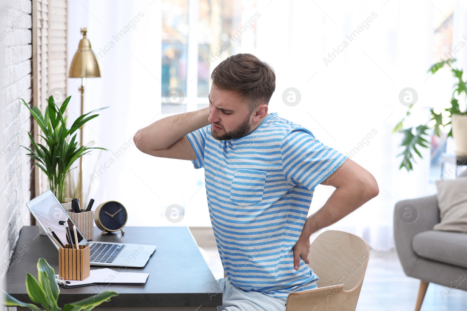 Photo of Young man suffering from back pain in office