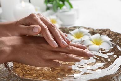 Photo of Woman soaking her hands in bowlwater and flowers on table, closeup with space for text. Spa treatment