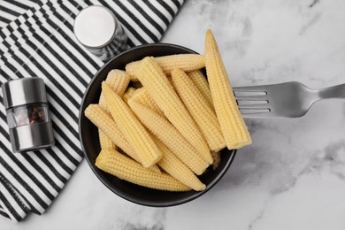 Photo of Bowl of pickled baby corn, pepper shaker and fork on white marble table, flat lay