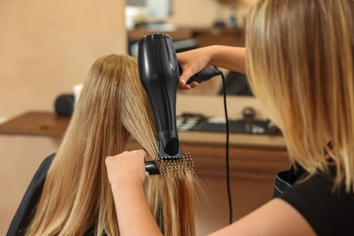 Professional hairdresser drying girl's hair in beauty salon, closeup