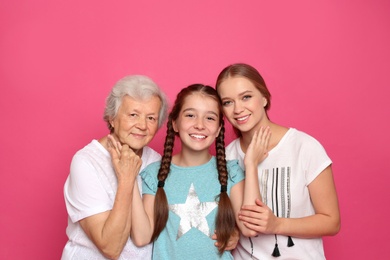Happy sisters with their grandmother on pink background