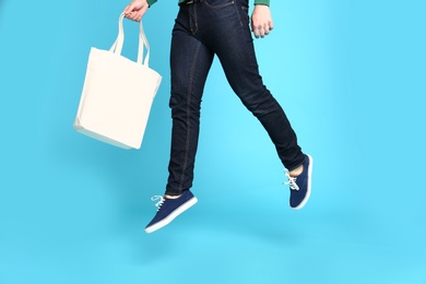 Young man with eco bag jumping on blue background, closeup