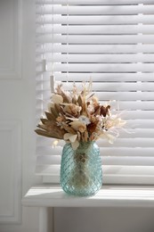 Photo of Beautiful dried flower bouquet in glass vase on white windowsill