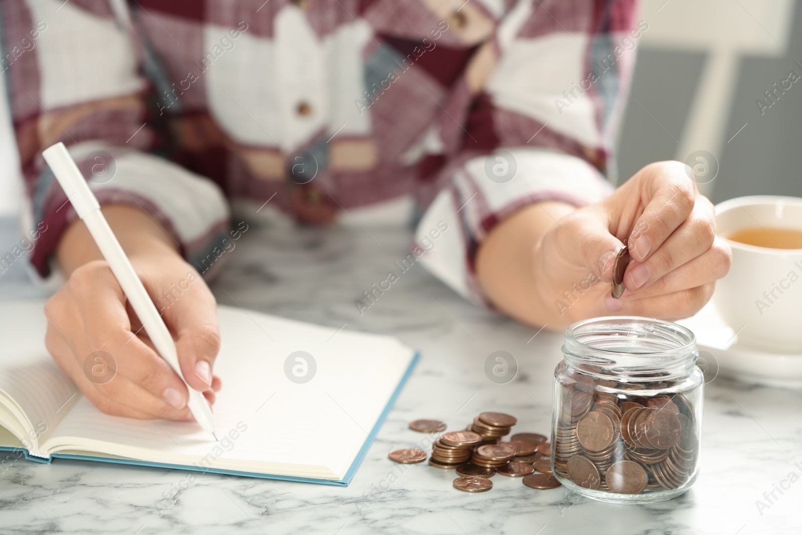 Photo of Woman putting money into glass jar at white marble table, closeup