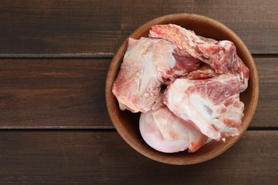 Photo of Bowl with raw chopped meaty bones on wooden table, top view. Space for text