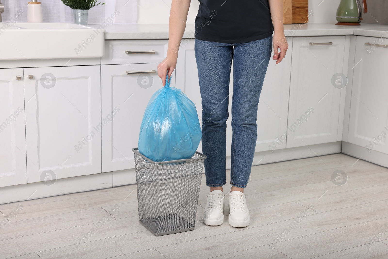 Photo of Woman taking garbage bag out of trash bin in kitchen, closeup