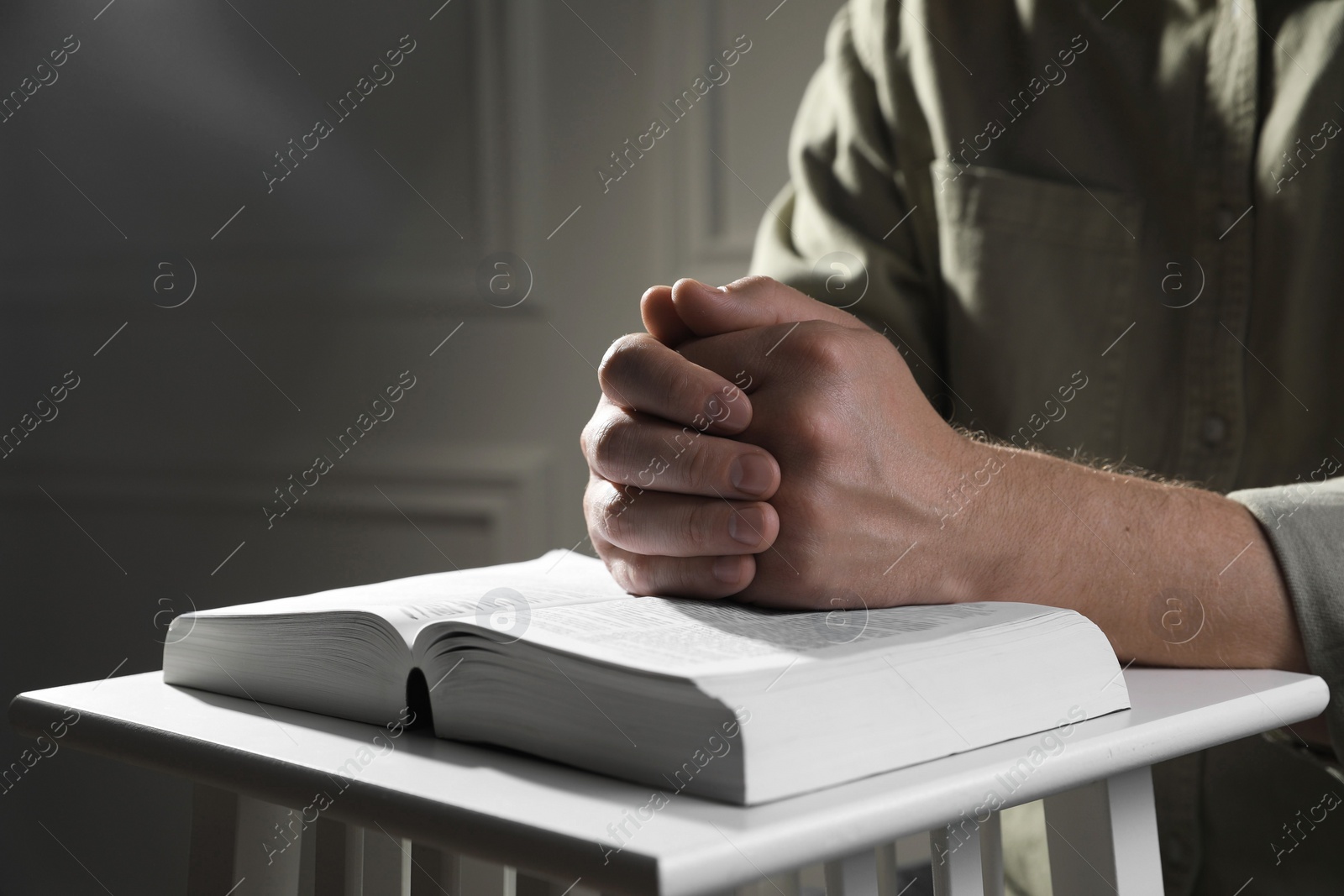 Photo of Religion. Christian man praying over Bible indoors, closeup