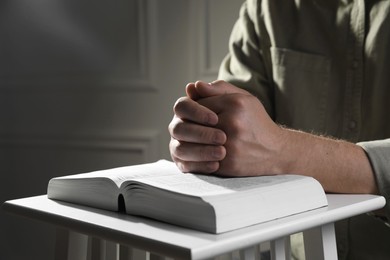 Photo of Religion. Christian man praying over Bible indoors, closeup