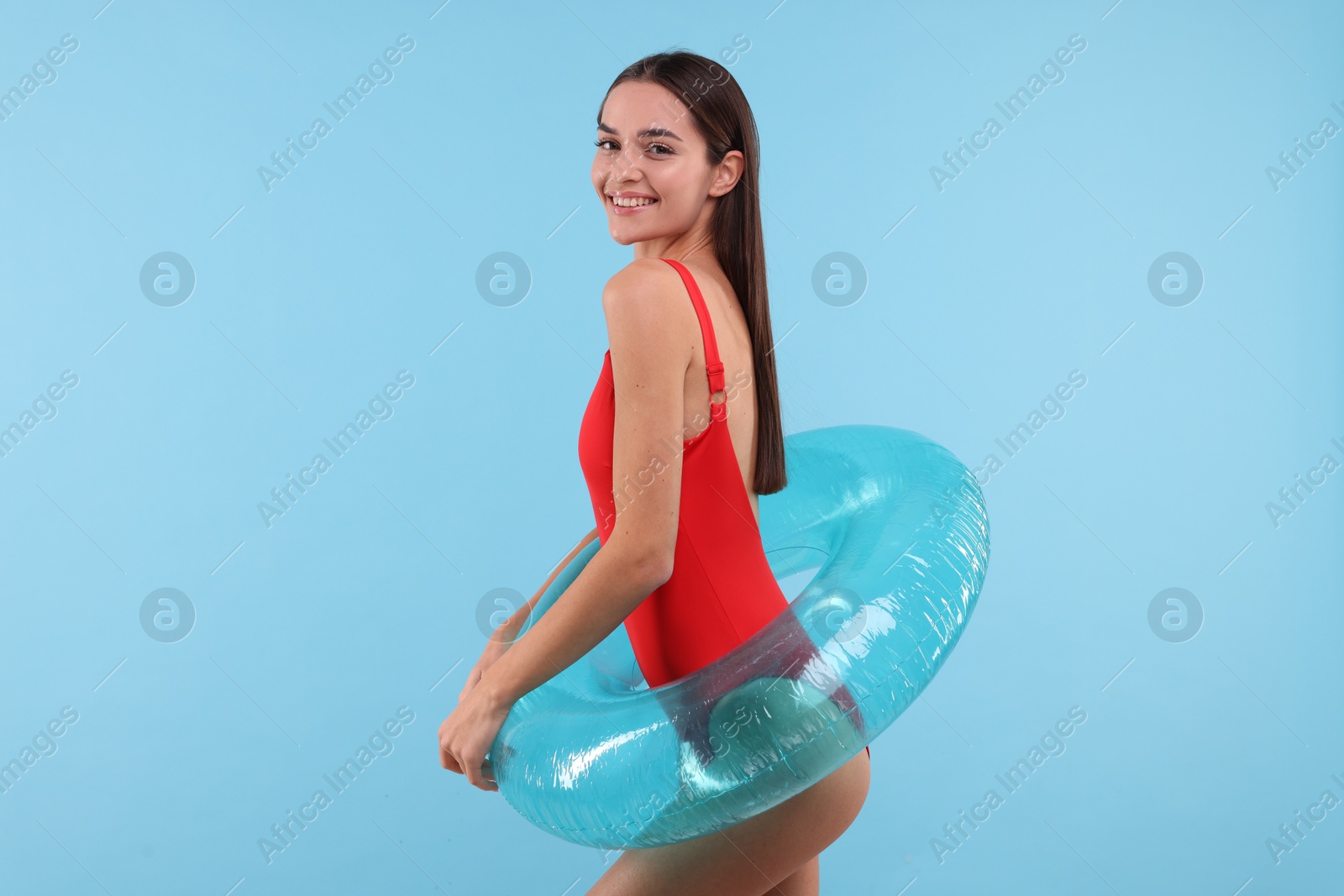 Photo of Young woman in stylish swimsuit with inflatable ring on light blue background