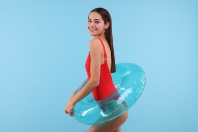 Photo of Young woman in stylish swimsuit with inflatable ring on light blue background
