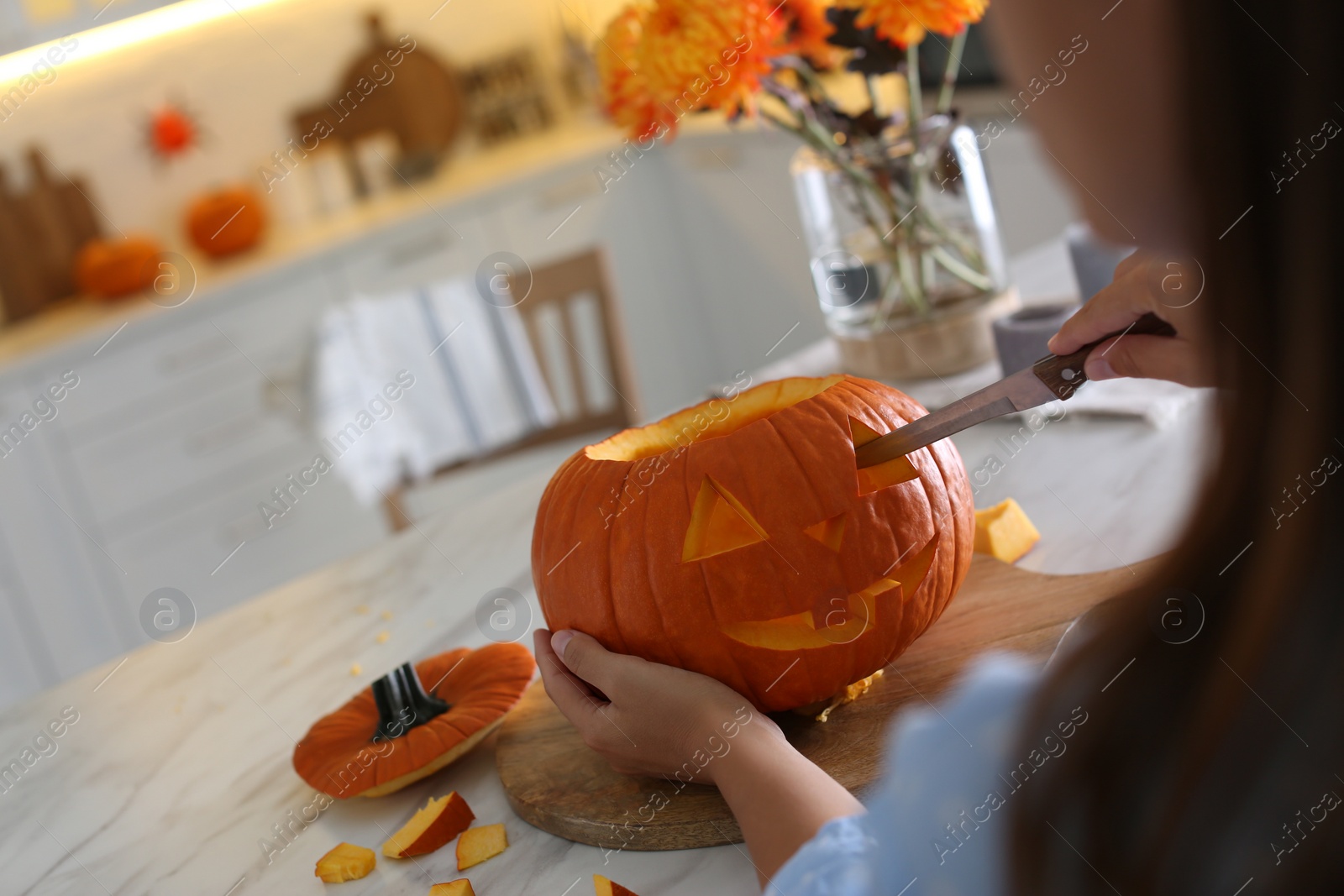 Photo of Woman making pumpkin jack o'lantern at table in kitchen, closeup. Halloween celebration