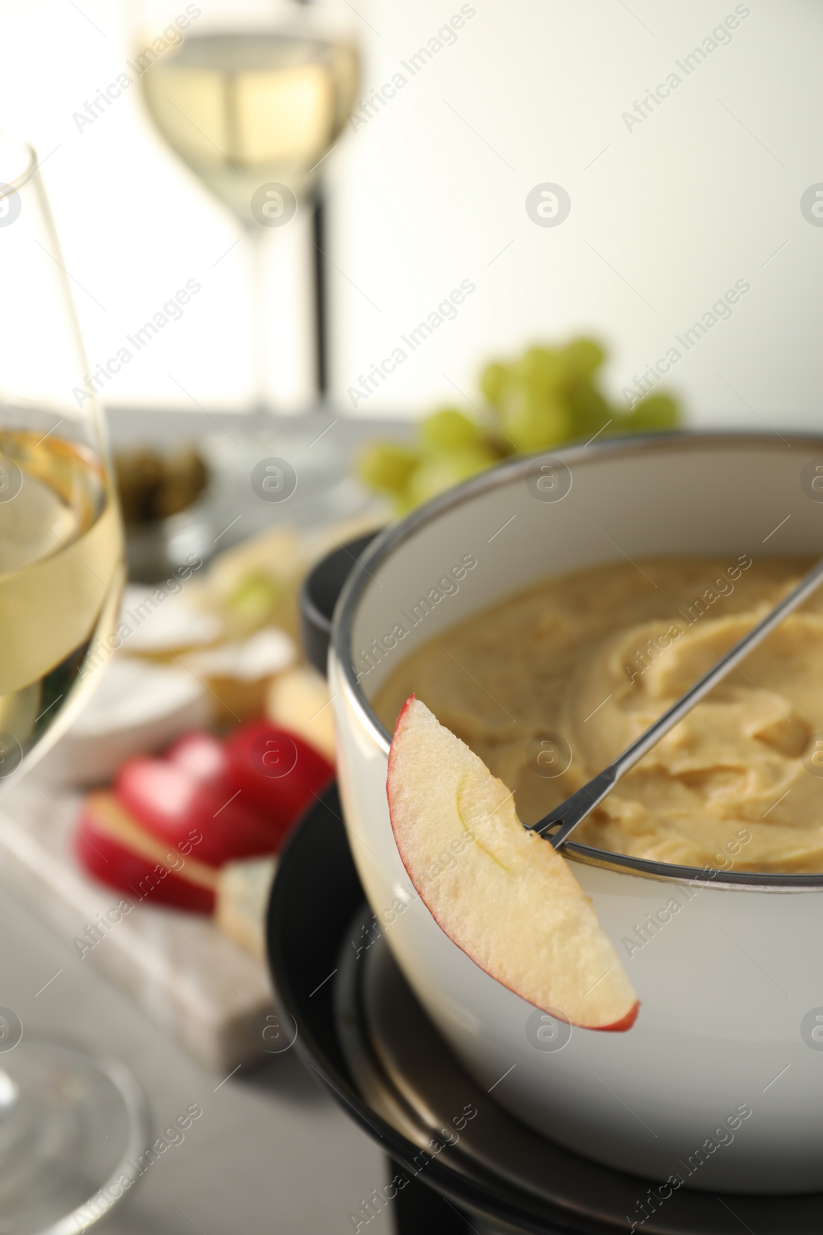 Photo of Fork with piece of apple and melted cheese in fondue pot on grey table, closeup