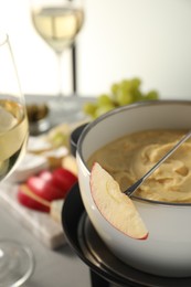 Fork with piece of apple and melted cheese in fondue pot on grey table, closeup