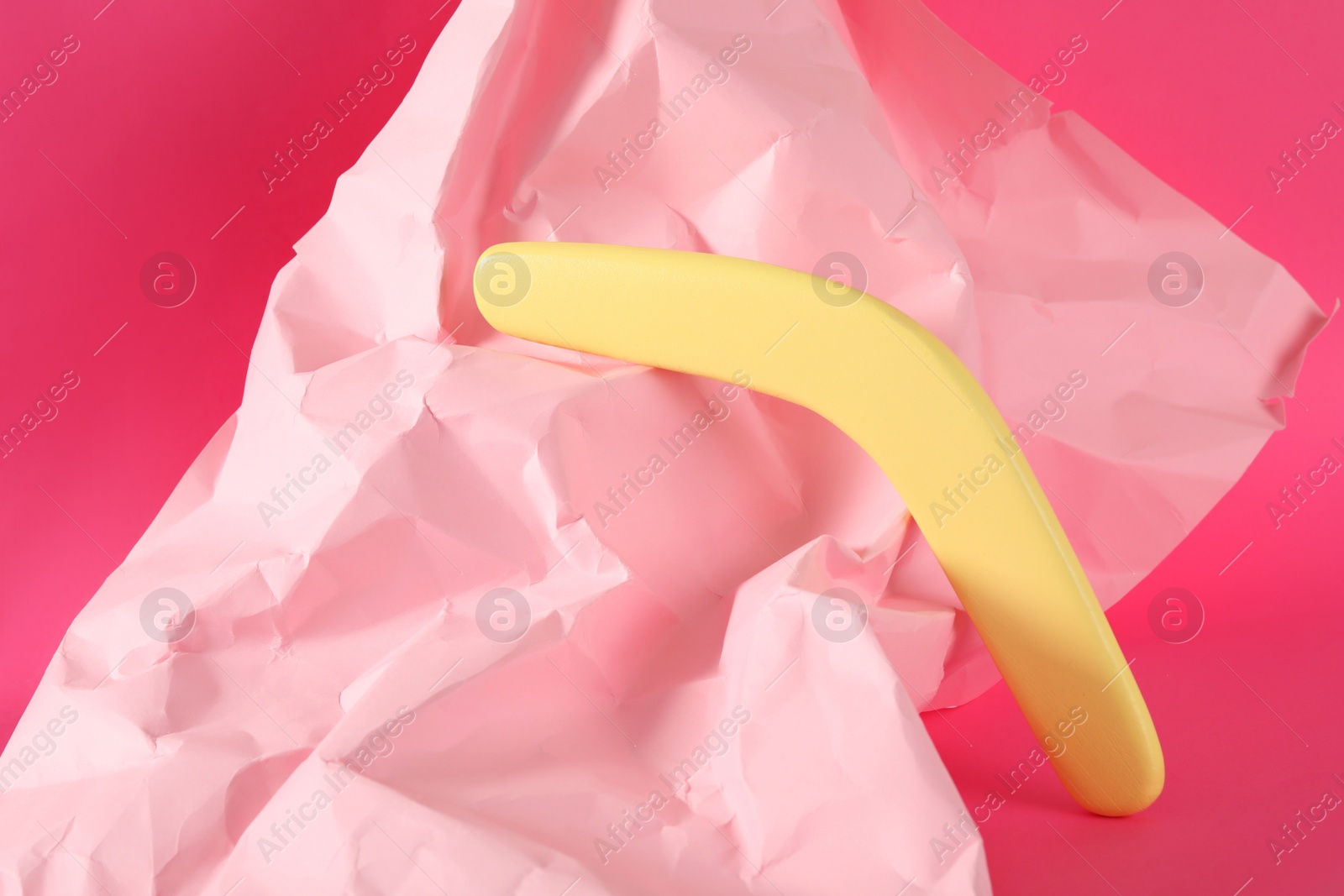 Photo of Creative composition with yellow wooden boomerang on pink background