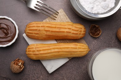 Photo of Delicious eclairs, chocolate paste and walnuts on grey table, flat lay