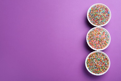 Photo of Colorful sprinkles in bowls on purple background, flat lay with space for text. Confectionery decor