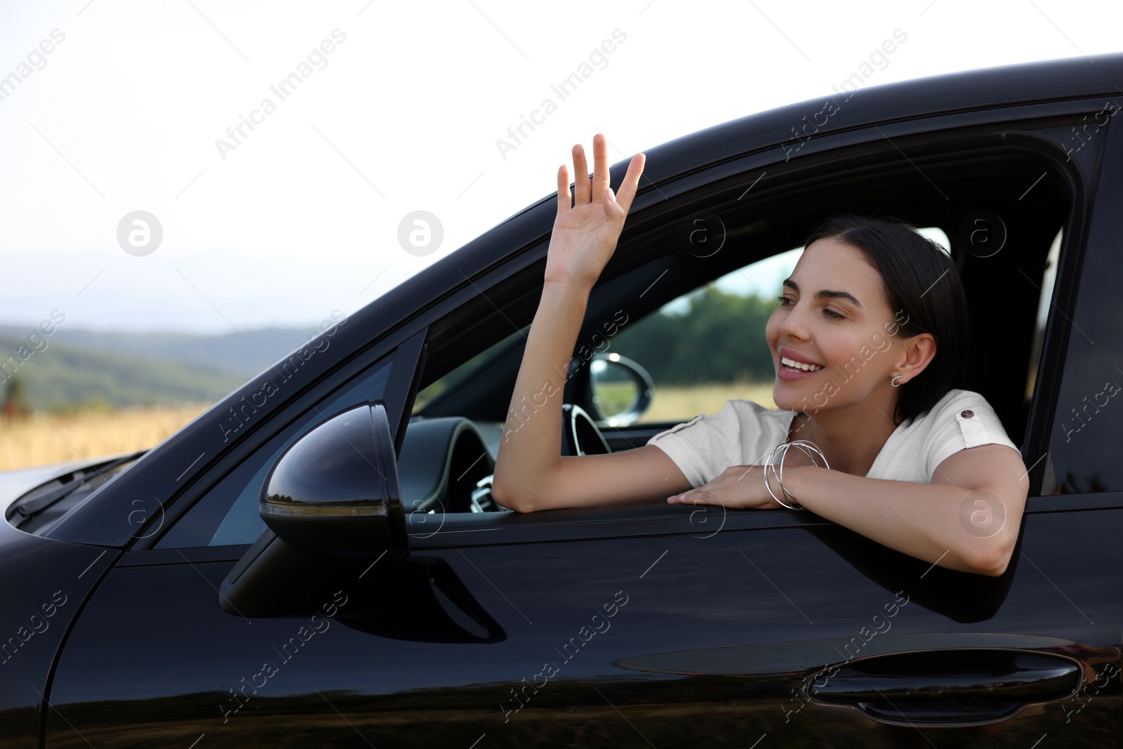 Photo of Enjoying trip. Portrait of beautiful happy woman waving in car, view from outside