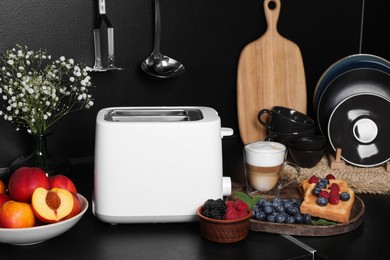 Modern toaster, bread, fresh berries and coffee on black table