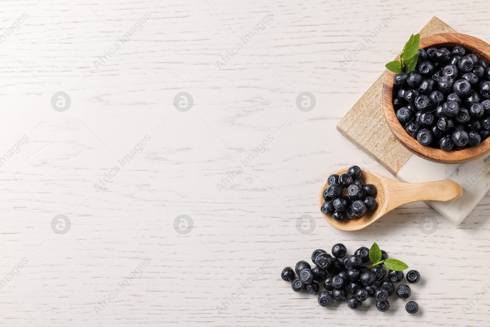 Photo of Ripe bilberries and leaves on white wooden table, flat lay. Space for text