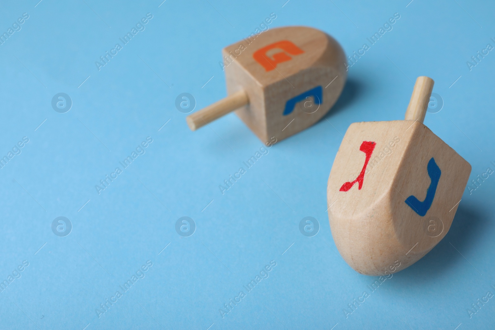Photo of Hanukkah traditional dreidels with letters Gimel, Nun and Pe on light blue background, space for text