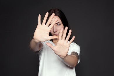 Young woman making stop gesture against dark background, focus on hand